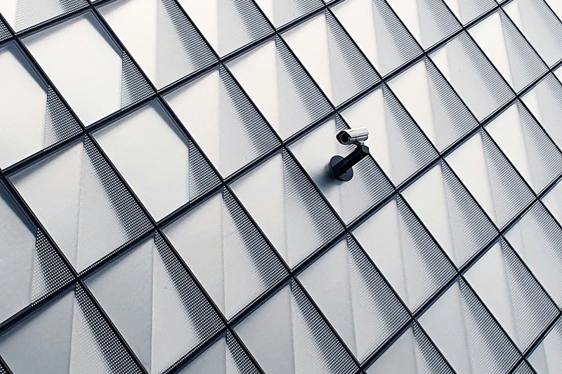 A textured wall of interlocking diamond shapes features a security camera, symbolizing modern surveillance and safety measures in policing and community monitoring efforts.