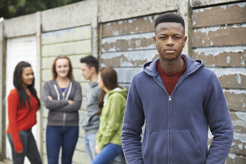 Group Of teenagers Hanging Out In Urban Environment, with black youth at the front looking straight at the camera